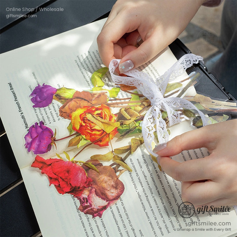 Hands arranging pressed rose stickers with lace ribbon on an open book