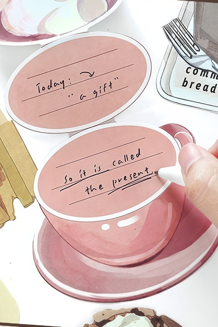Pink ceramic teacup and saucer with handwritten text paired with matching oval notecard on a light artistic background