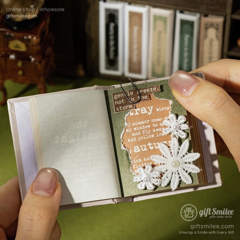Miniature open scrapbook with green and brown pages white lace floral appliqus and a silver paperclip detail