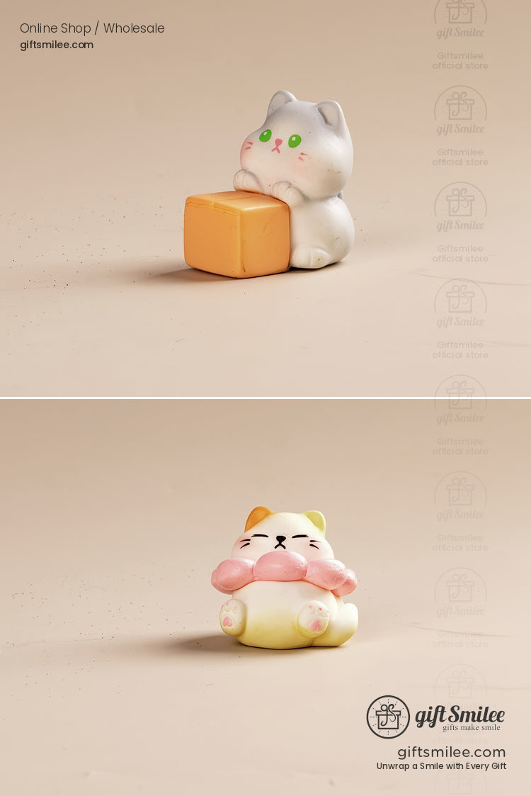 Two pastel ceramic cat figurines one gray holding an orange cube the other yellow with a pink scarf on a beige surface