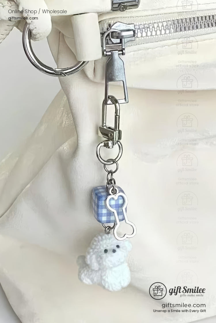 White quilted bag with a silver zipper featuring a charm of a blue gingham cube bone pendant and plush white poodle