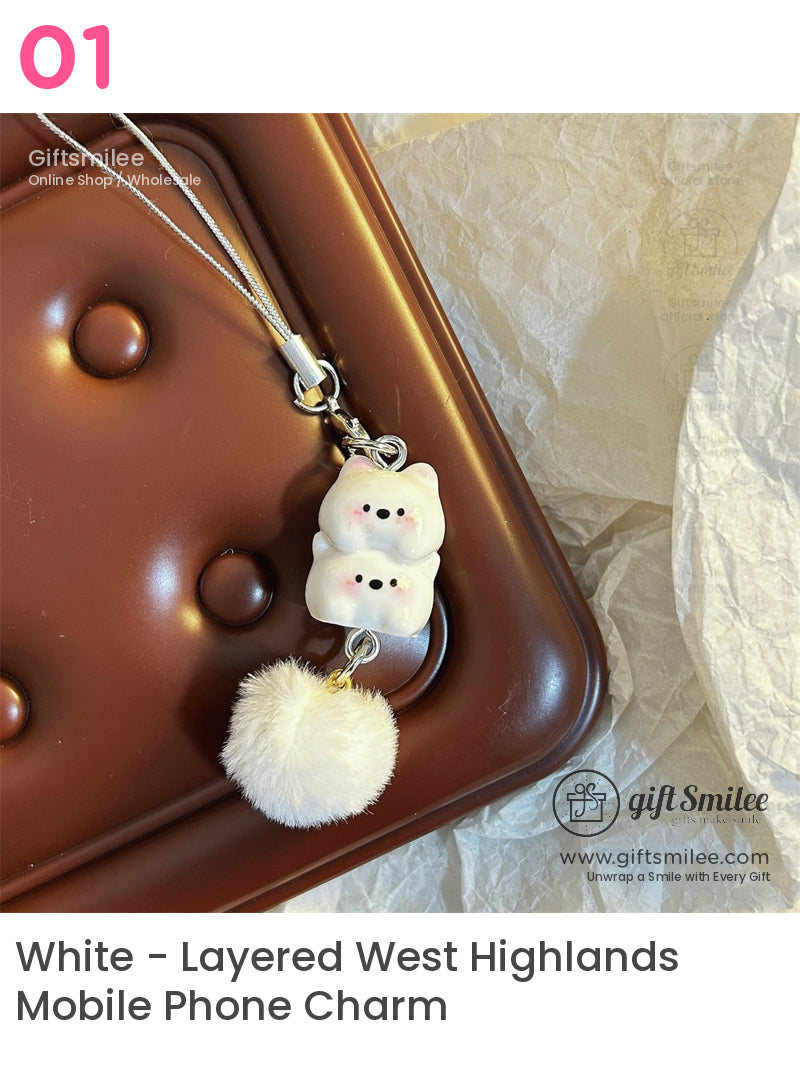 White ceramic cat charm with rosy cheeks fluffy white pompom and silver chain on a brown textured surface