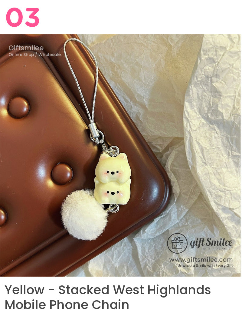 Creamy yellow twin bear charm with black details fluffy white pompom attached to silver strap on brown textured surface