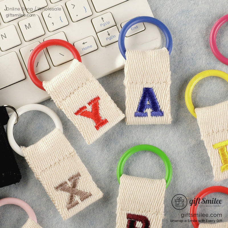 Multicolored embroidered alphabet keyrings with beige canvas tabs and vibrant circular rings on a light surface