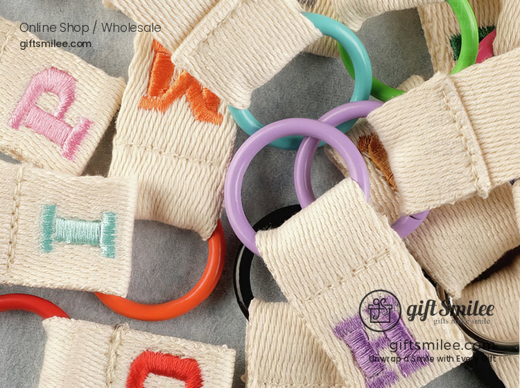 Beige woven fabric keychains with colorful embroidered letters and vibrant plastic rings in assorted shades