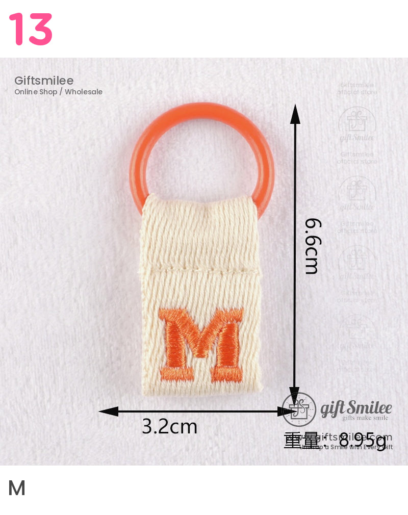 Cream cotton keychain tag with orange embroidered M and circular orange ring measuring 66cm by 32cm