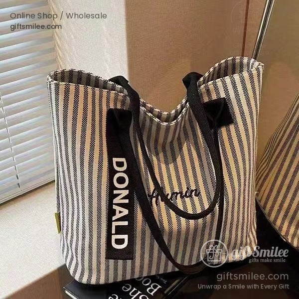 Black and white striped canvas tote bag with bold DONALD text black handles and minimal yellow accent