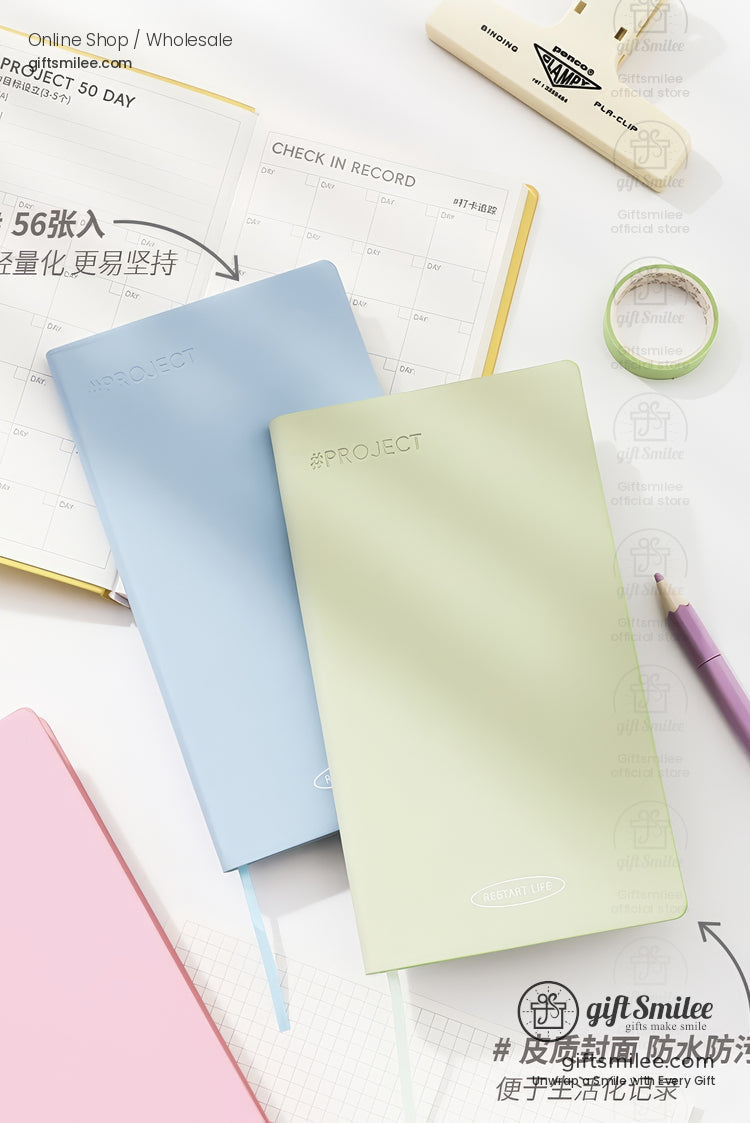 Pastel hardcover project notebooks in blue and light green on a desk with calendar planner, pen, and washi tape – minimalist stationery flat lay.