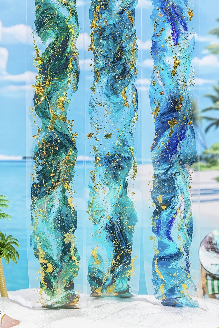 Three abstract resin sculptures in aqua blue and gold swirls with metallic accents displayed against a beach backdrop