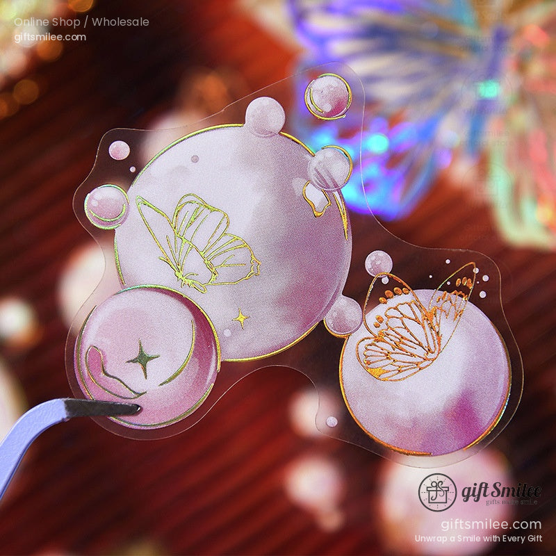 A detailed shot of pink bubble stickers with golden butterfly accents, held with precision tweezers