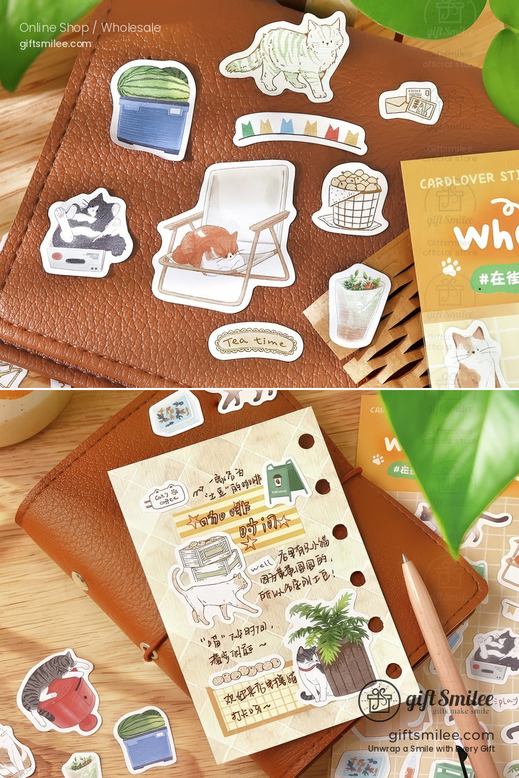 Assorted catthemed decorative stickers on a brown leather notebook with a beige journal and wooden desk accents