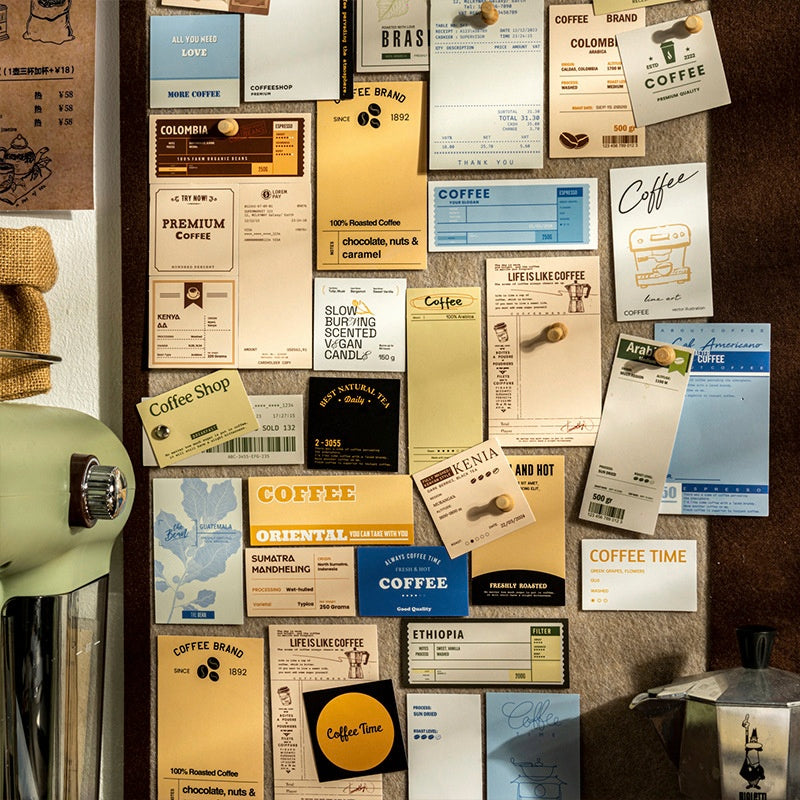 Assorted coffeethemed cards and labels in beige blue and yellow tones pinned on a corkboard with a retro green coffee grinder