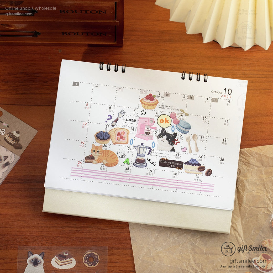 Spiralbound October desk calendar with colorful cat dessert and kitchenthemed stickers on a wooden surface