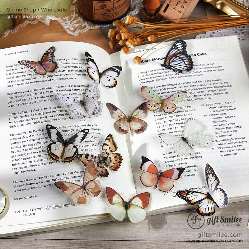 Assorted realistic butterfly stickers in soft pastel shades displayed on an open book with dried flowers nearby