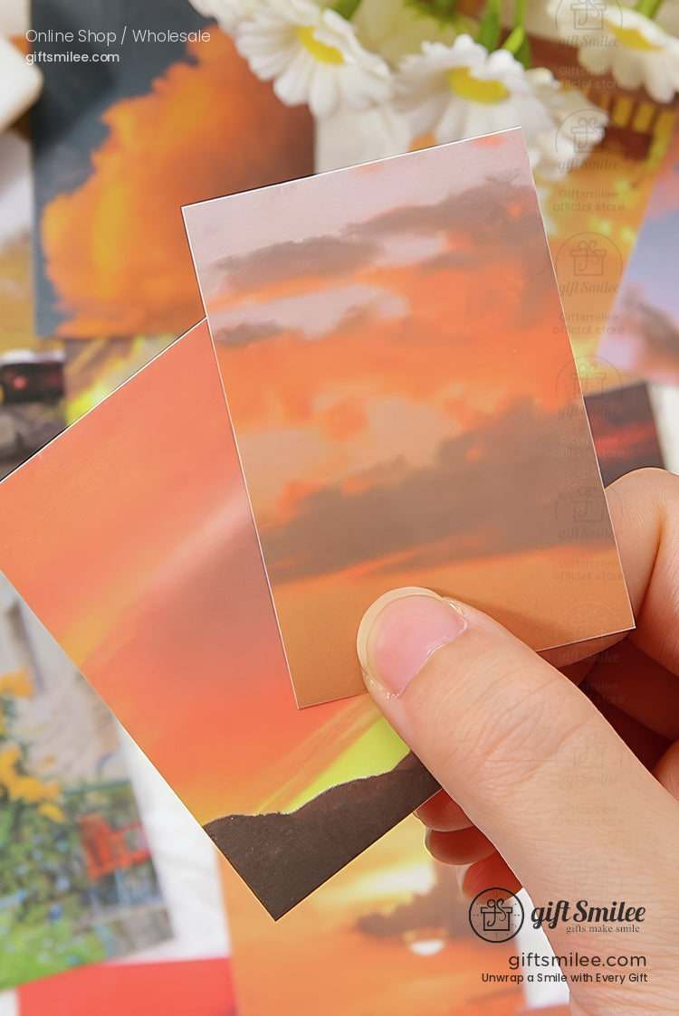 Glossy sunsetthemed photo cards with vivid orange and pink skies held by hand surrounded by floral accents