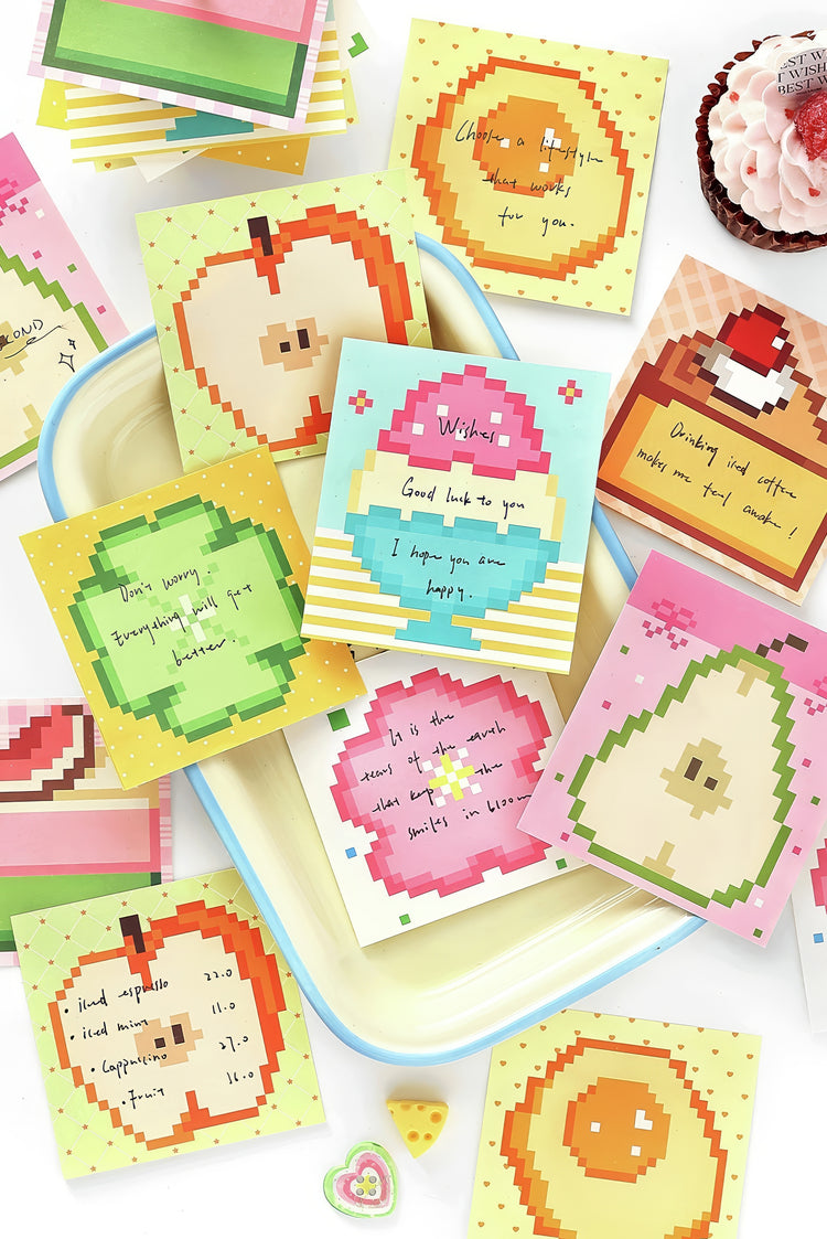Colorful pixel art greeting cards with fruit designs and handwritten messages displayed on a pastel tray